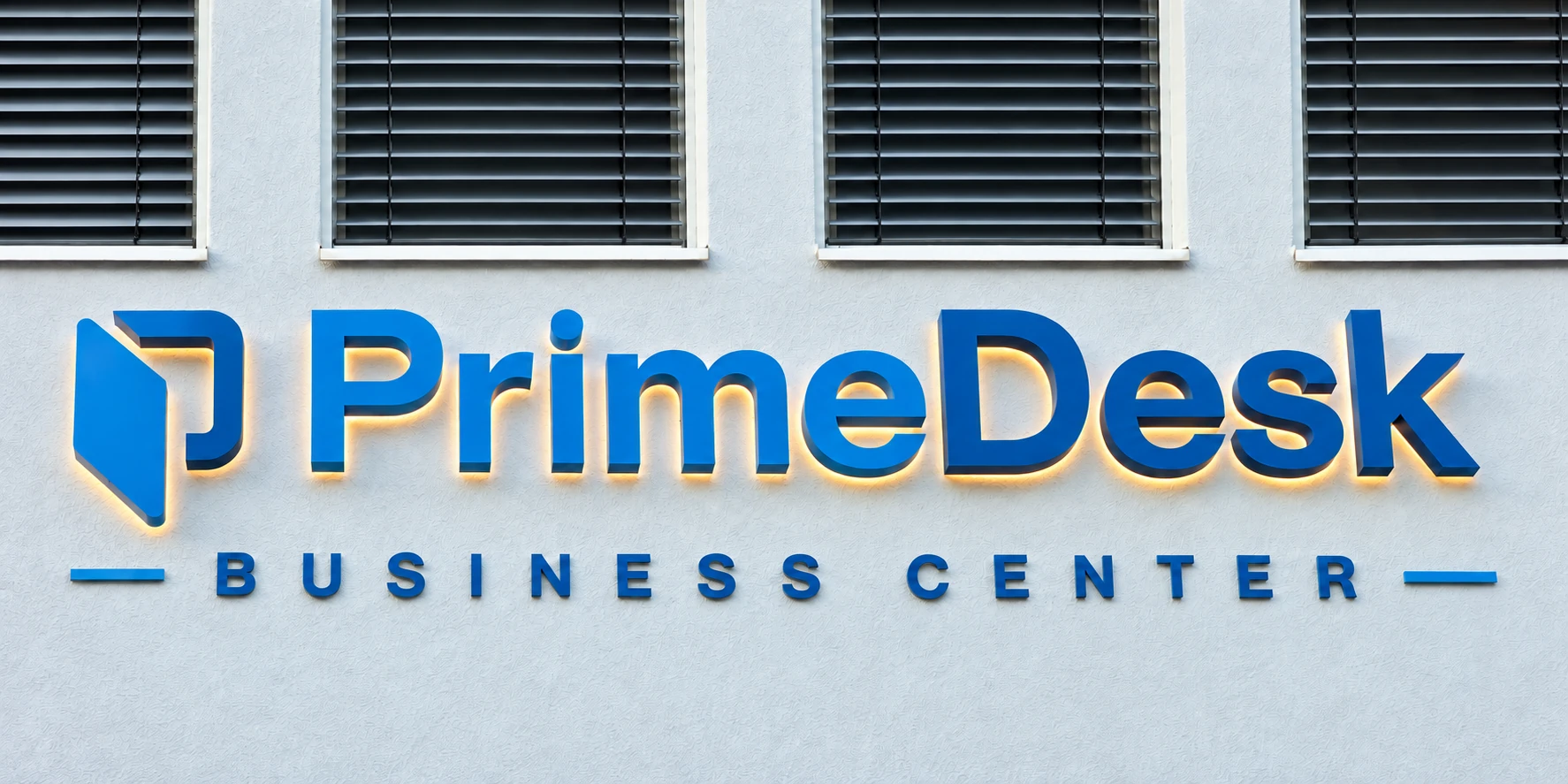 Blue PrimeDesk letters on the bright facade with subtle backlighting